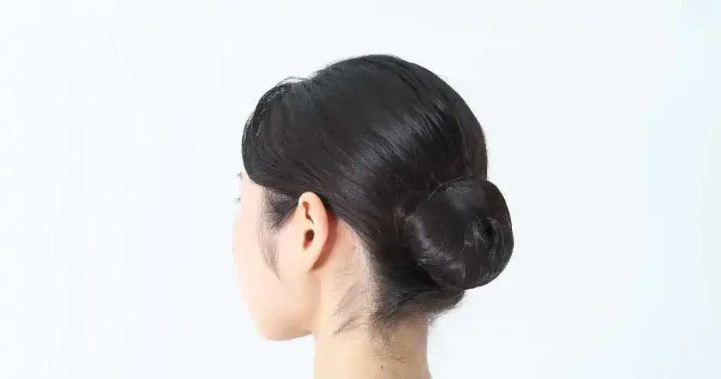 白い背景に映るシンプルなシニヨンヘアの女性の後ろ姿。面接当日にヘアスタイルで悩まないための準備方法を説明するセクションに関連するビジュアル。