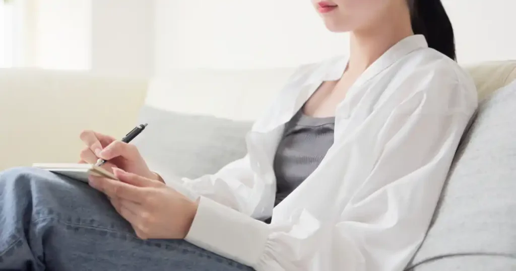 ソファに座ってノートにメモを取る女性の横顔。自己分析本を活用しても分析が上手くいかない理由について説明する記事セクションに関連したイメージ。