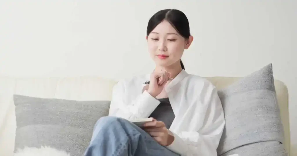 ソファに座ってノートを見ながら考え事をする女性。自己分析本を活用して転職活動を成功させるポイントについて説明するセクションに関連したイメージ。