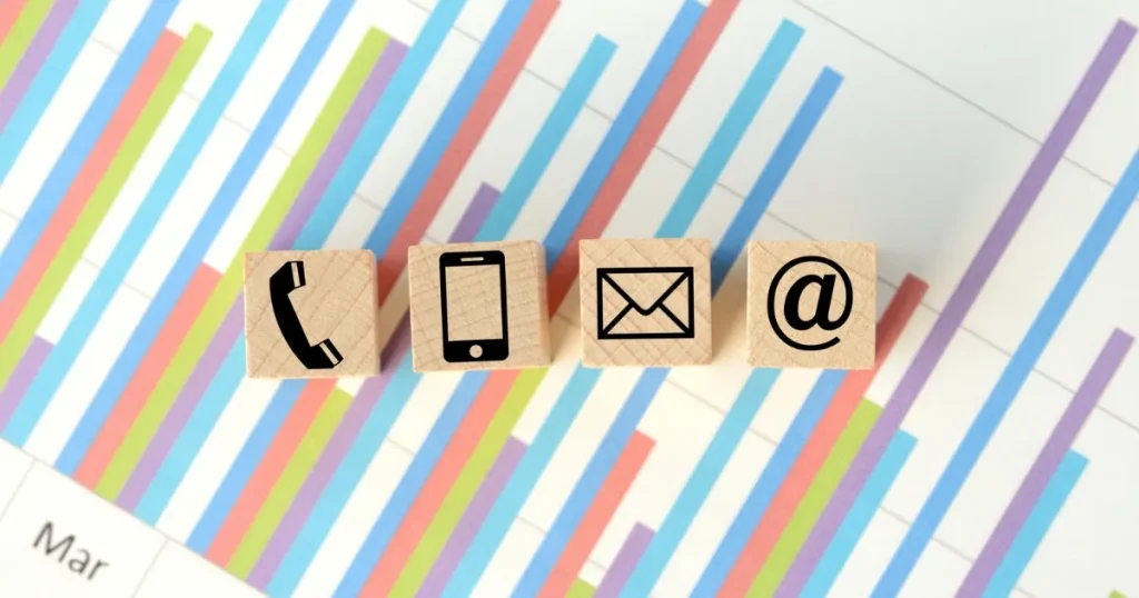 カラフルなグラフを背景に、メールや電話、スマートフォンのアイコンが描かれた木製のキューブが並ぶ。就活で企業へのフォローメールに関するポイントを説明するイメージ。