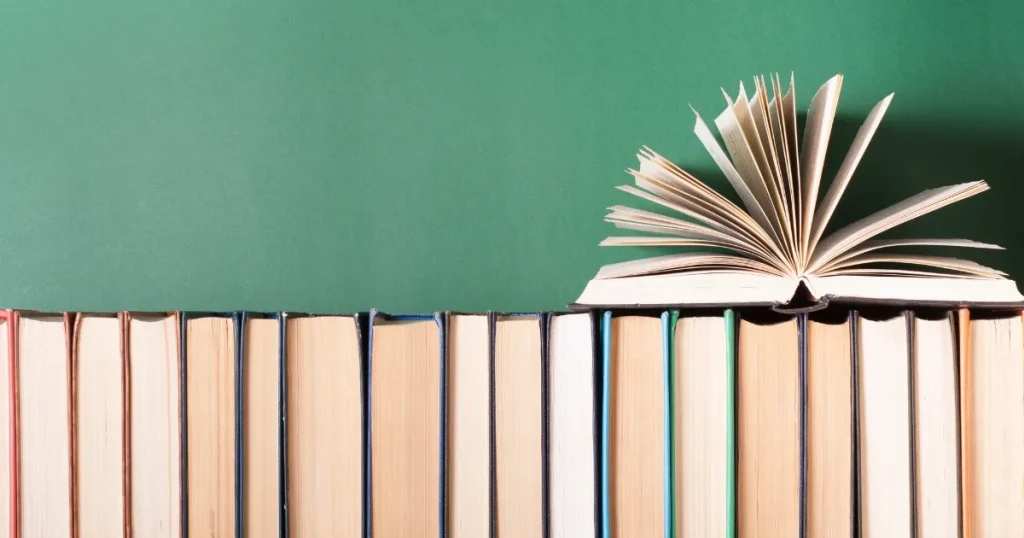 緑色の背景の前に並べられた複数の本と、開かれた1冊。自己分析を進めるために本を活用する手順を説明するセクションに関連したイメージ。