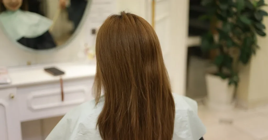 鏡の前に座るロングヘアの女性の後ろ姿。面接でロングヘアの髪型に悩む主な理由について説明するセクションに関連したイメージ。