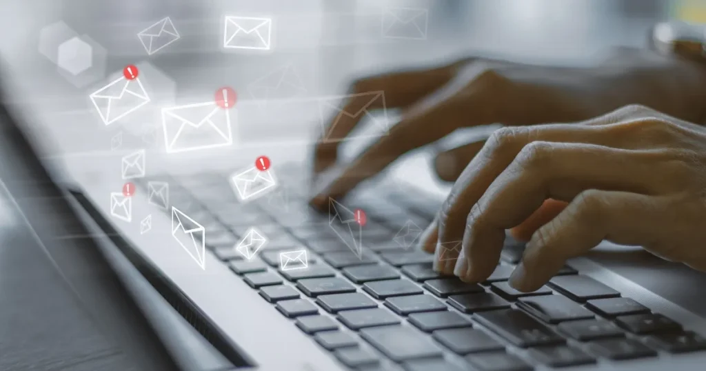 ノートパソコンのキーボードをタイピングする手元と、漂うメールアイコンのイメージ。面接日程変更メールの基本構成について解説するセクションに関連したビジュアル。