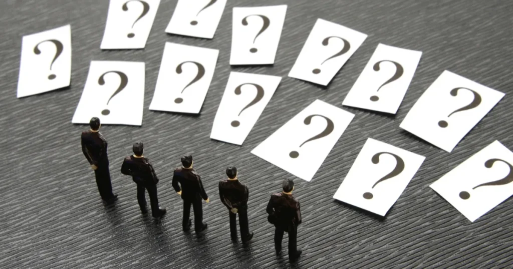 クエスチョンマークが描かれた多数のカードと、それを見つめる小さなビジネスマンのフィギュア。企業が逆質問の時間を設ける理由を象徴するイメージ。